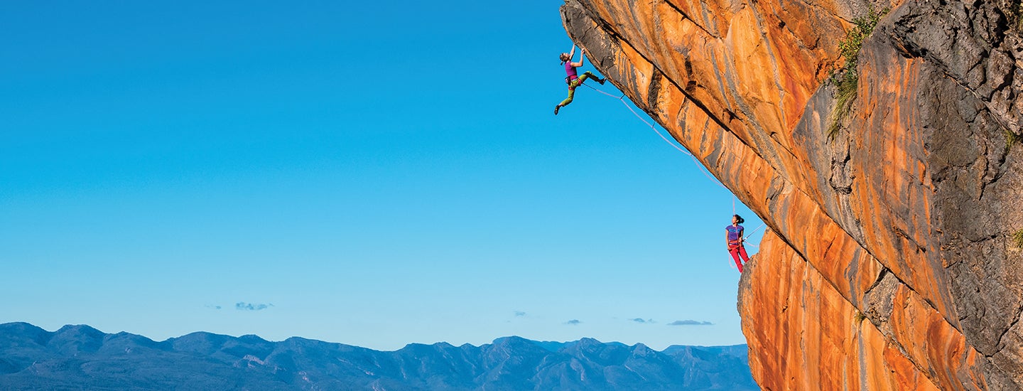 Two people climbing a cliff